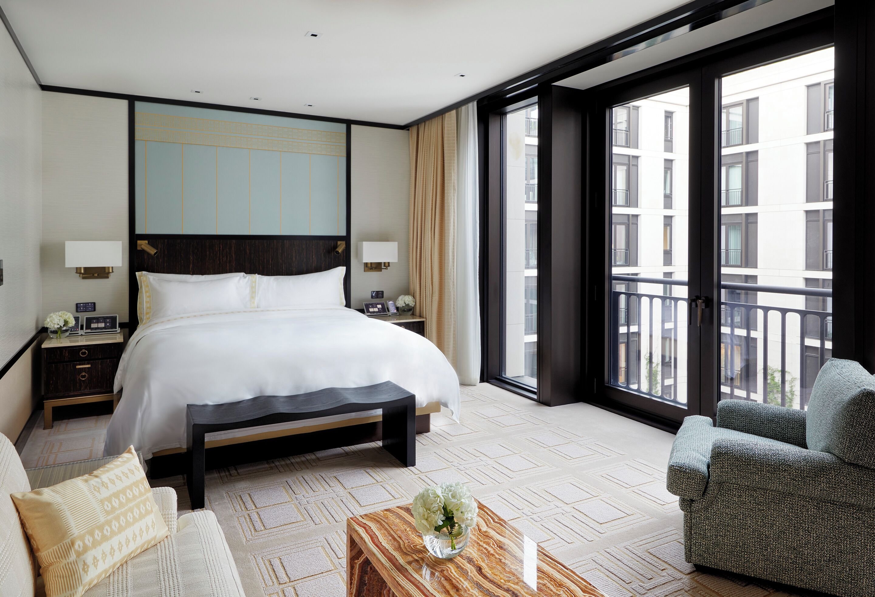 Une chambre d’hôtel avec un grand lit, des tables de chevet, un canapé, une table basse et une vue sur la ville grâce à de grandes fenêtres.