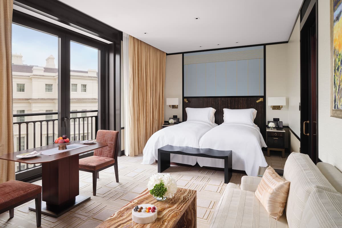 A hotel room with a large bed, a desk, a chair, a sofa, and a view of buildings through a large window.