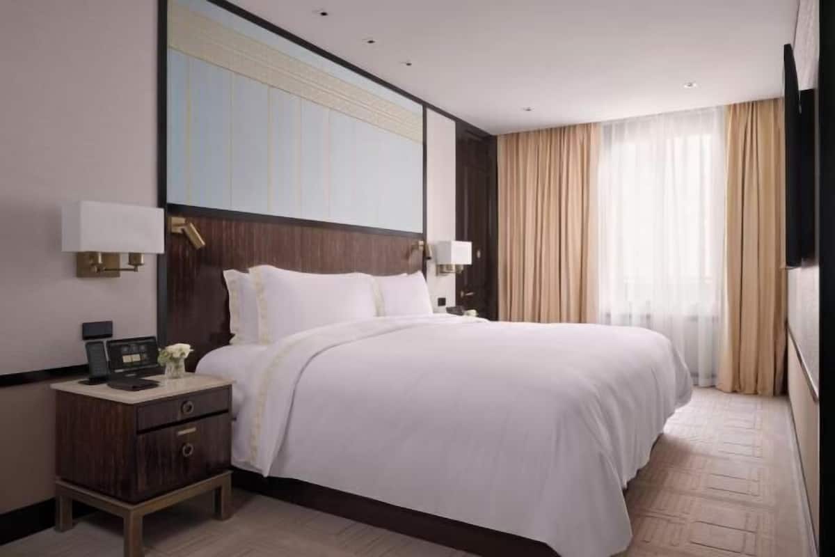 A hotel room with a large bed, bedside lamps, a nightstand, and a television.