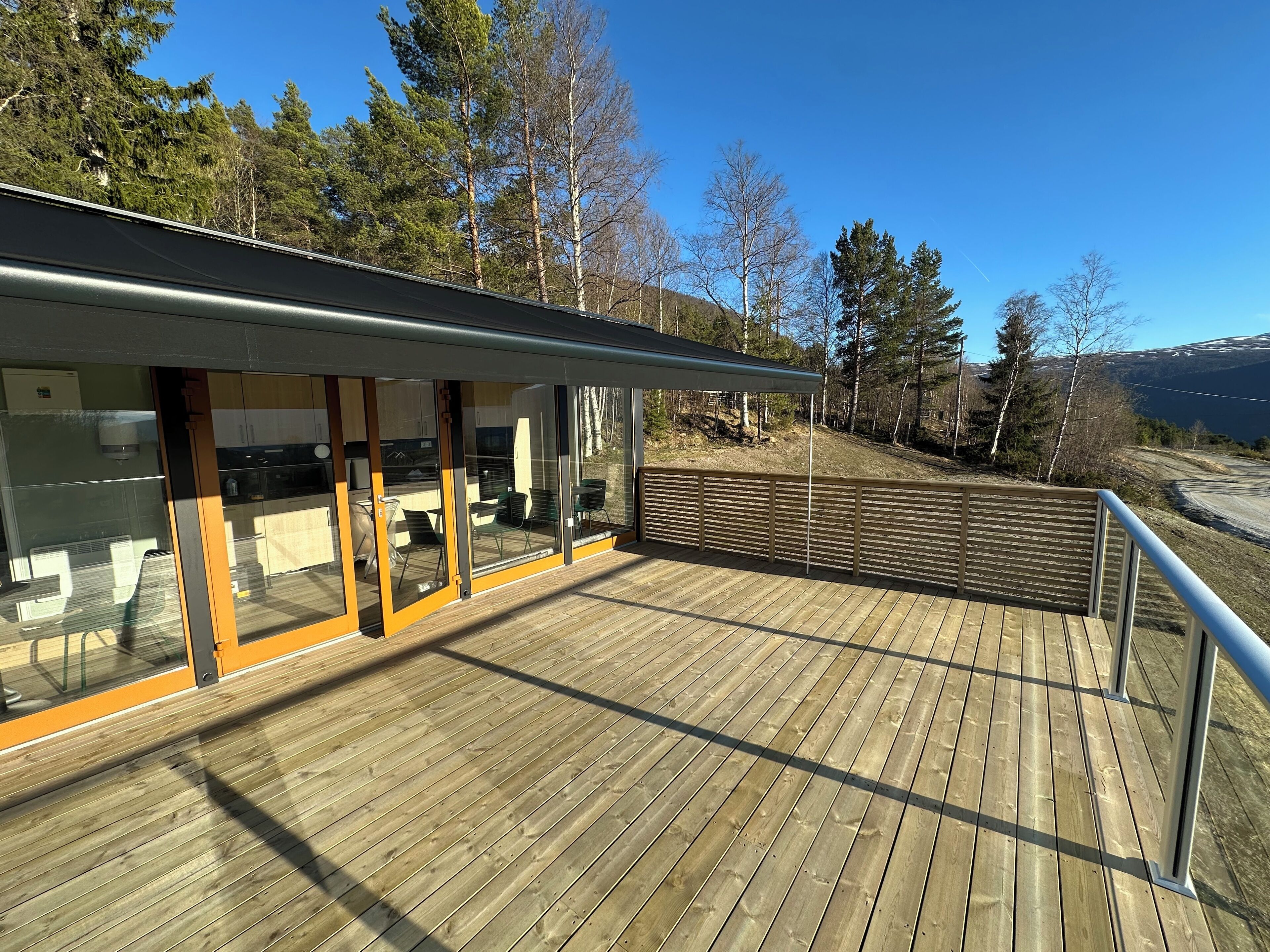 Une terrasse extérieure moderne dotée d’un espace cuisine, comprenant des placards et une table à manger, et offrant une vue sur un paysage boisé.