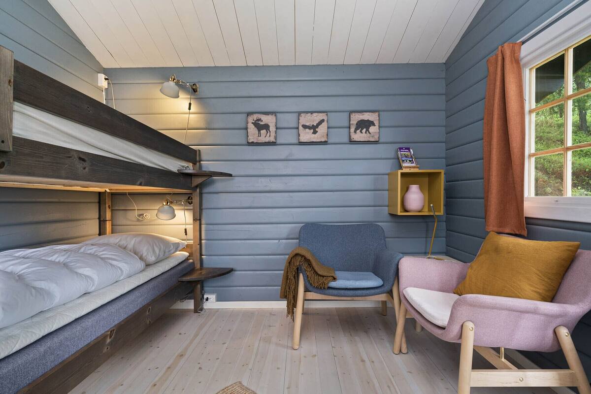 Ein gemütliches Zimmer mit einem Etagenbett, einem blauen Sessel, einem rosa Sessel und einem kleinen Regal mit einer Vase.