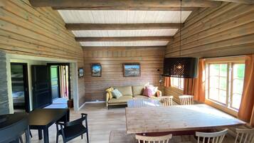 Een houten chalet van binnen, met een eettafel, stoelen, een bank en een televisie.