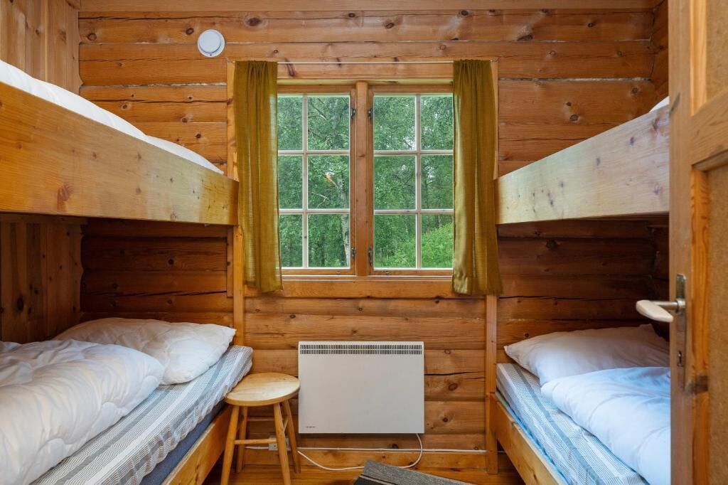 Eine Hütte mit zwei Etagenbetten, einem fenster mit Vorhängen und einem weißen Heizgerät.