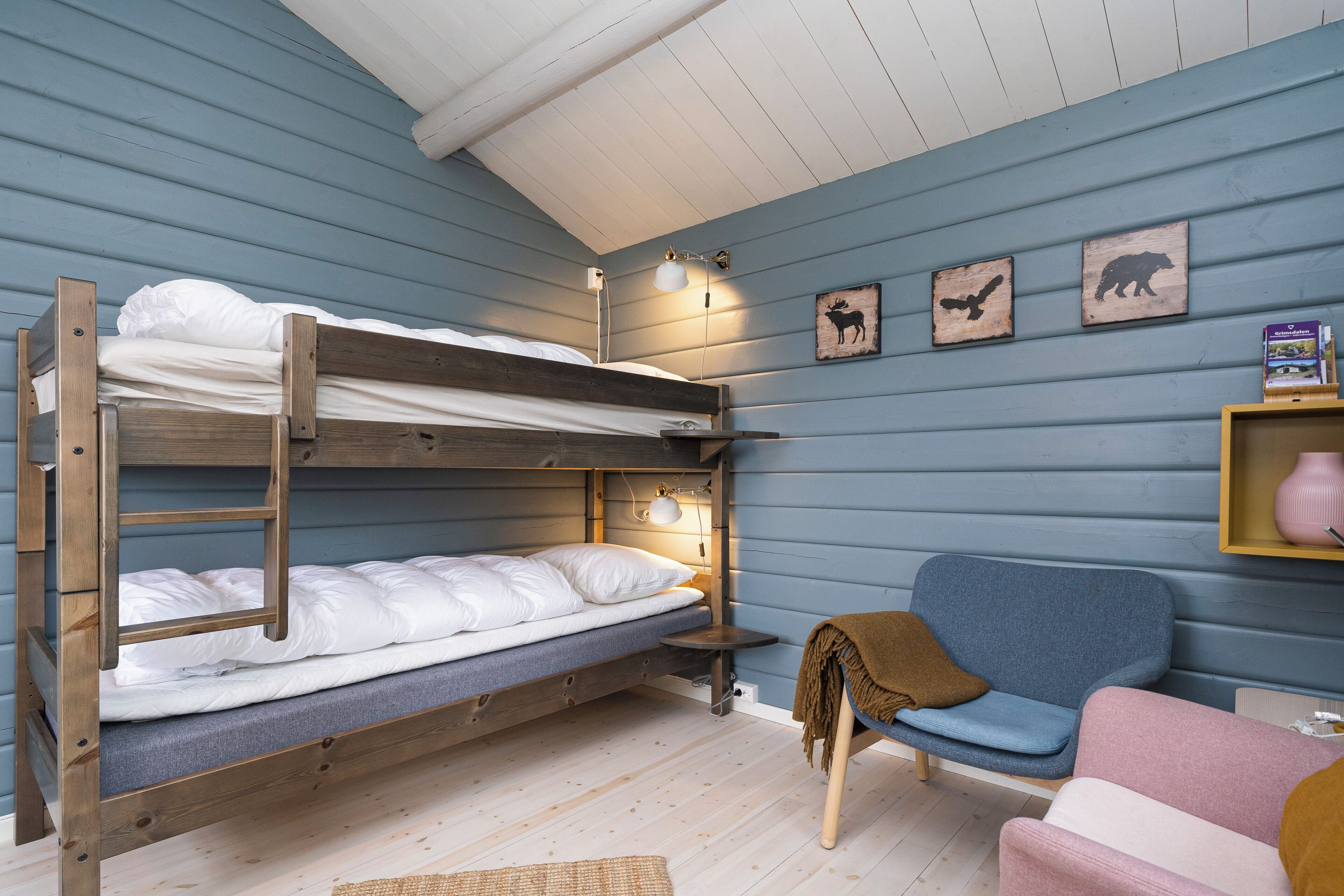 A bunk bed with a headboard, a bedside table with a lamp, a blue chair, and a pink chair.