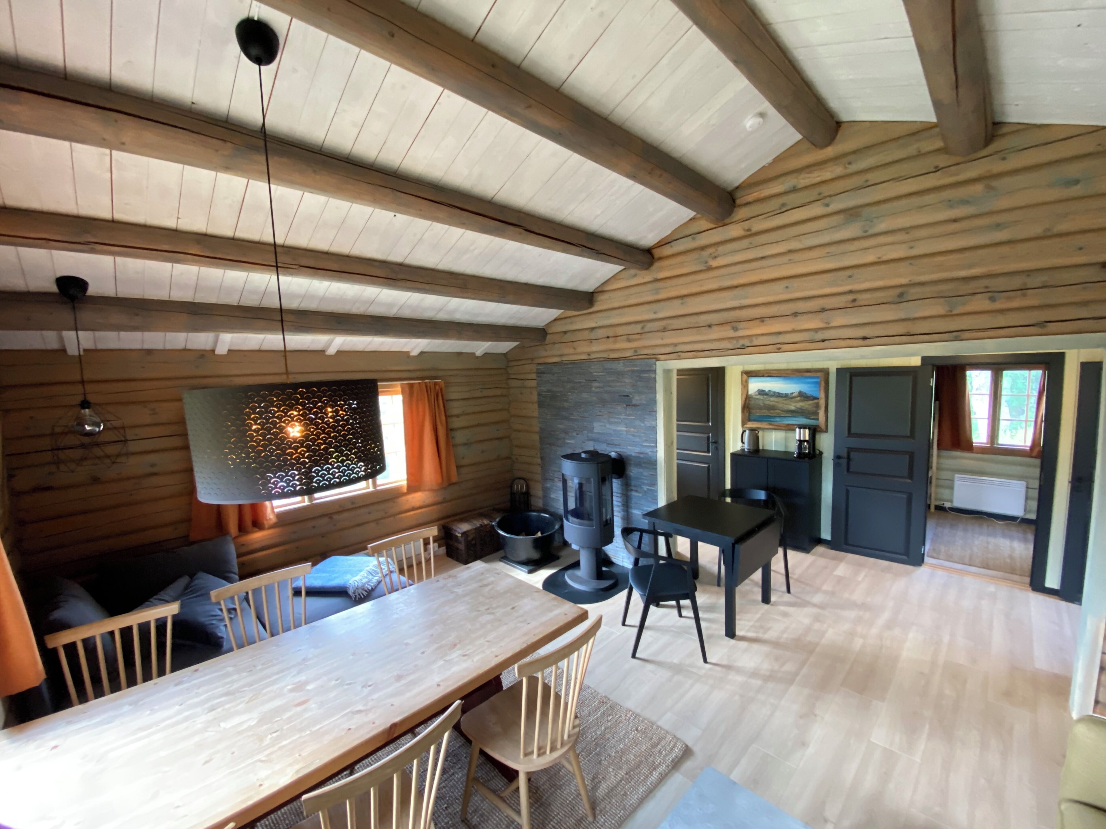 A cozy cabin interior with a wooden dining table, chairs, a fireplace, and a kitchen area.