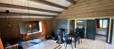 A cozy cabin interior with a wooden dining table, chairs, a fireplace, and a kitchen area.