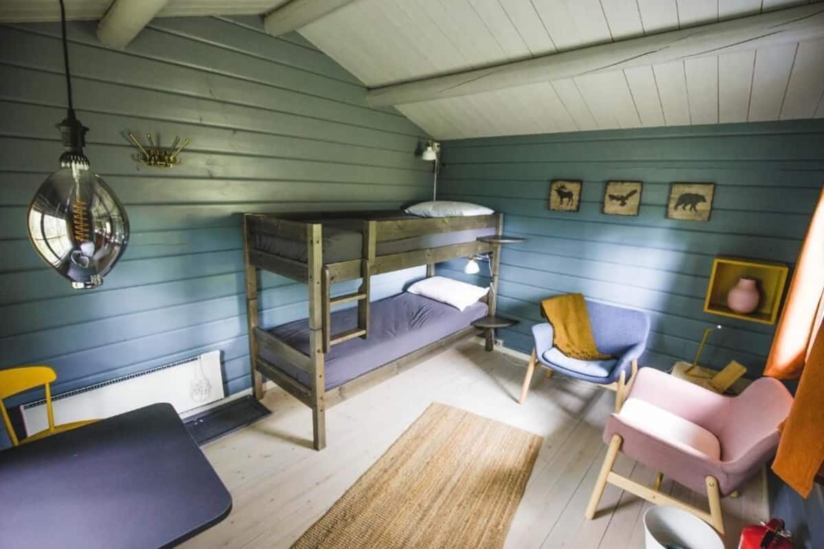 Ein Mehrbettzimmer mit Schreibtisch, Stuhl und kleinem Tisch. An den Wänden sind Dekorationen angebracht und es gibt eine Pendelleuchte.