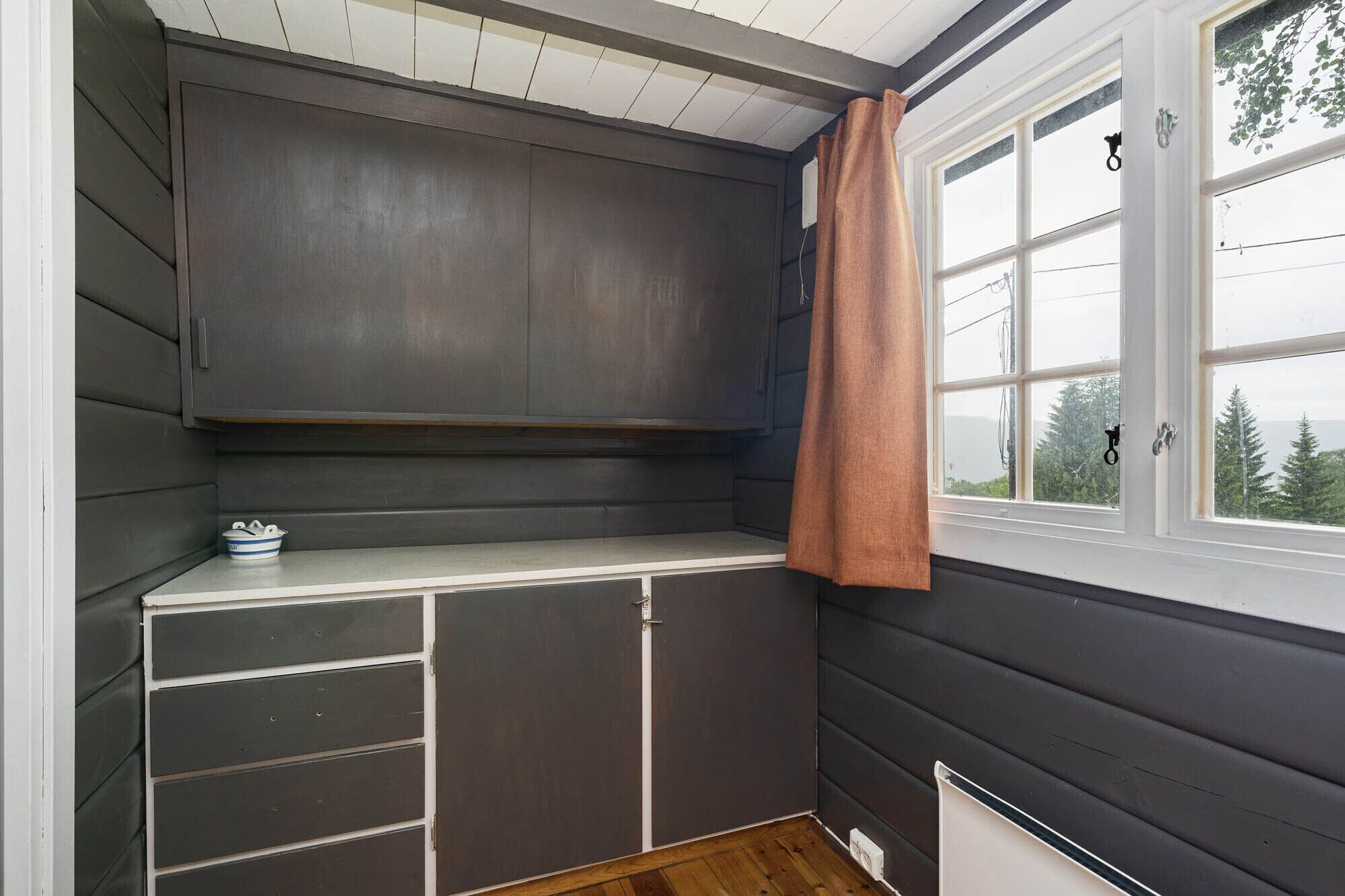 A room with a built-in bench, a window with a view of trees, and a door with a curtain.