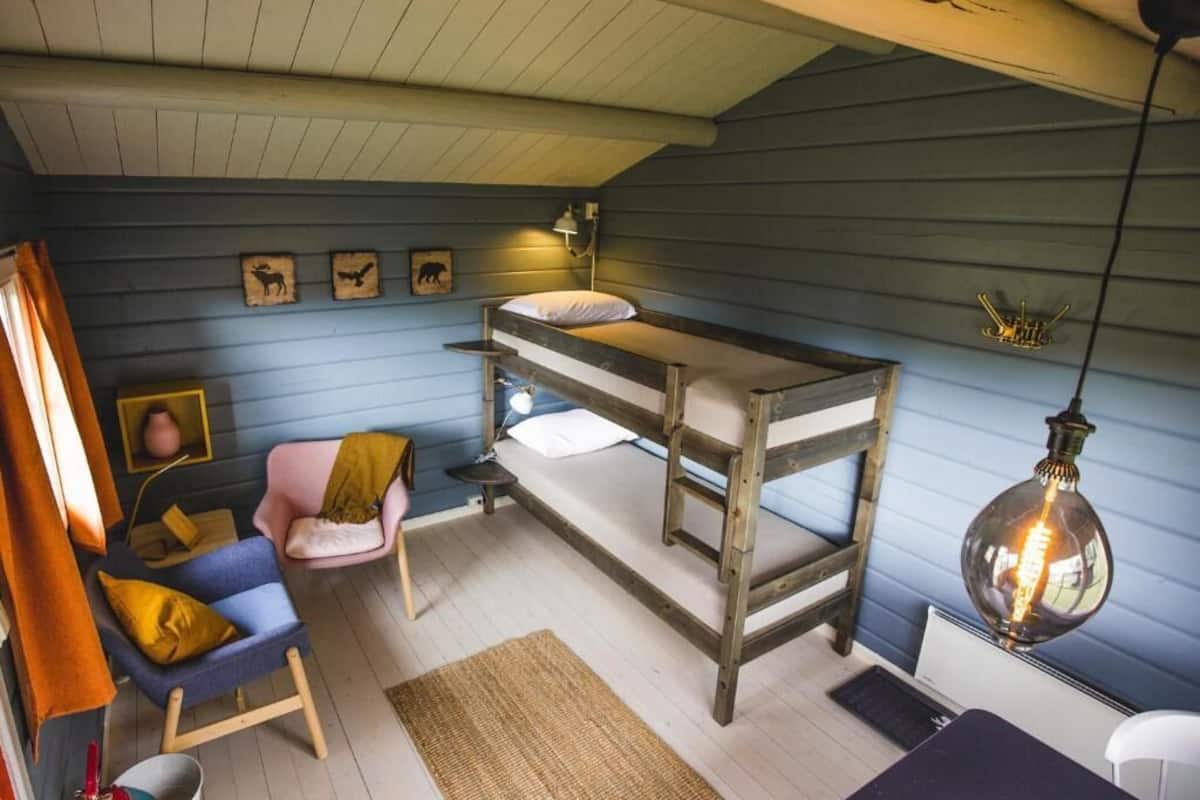Ein gemütliches Zimmer mit einem Etagenbett, einem Sessel, einem Schreibtisch und einer Pendelleuchte.