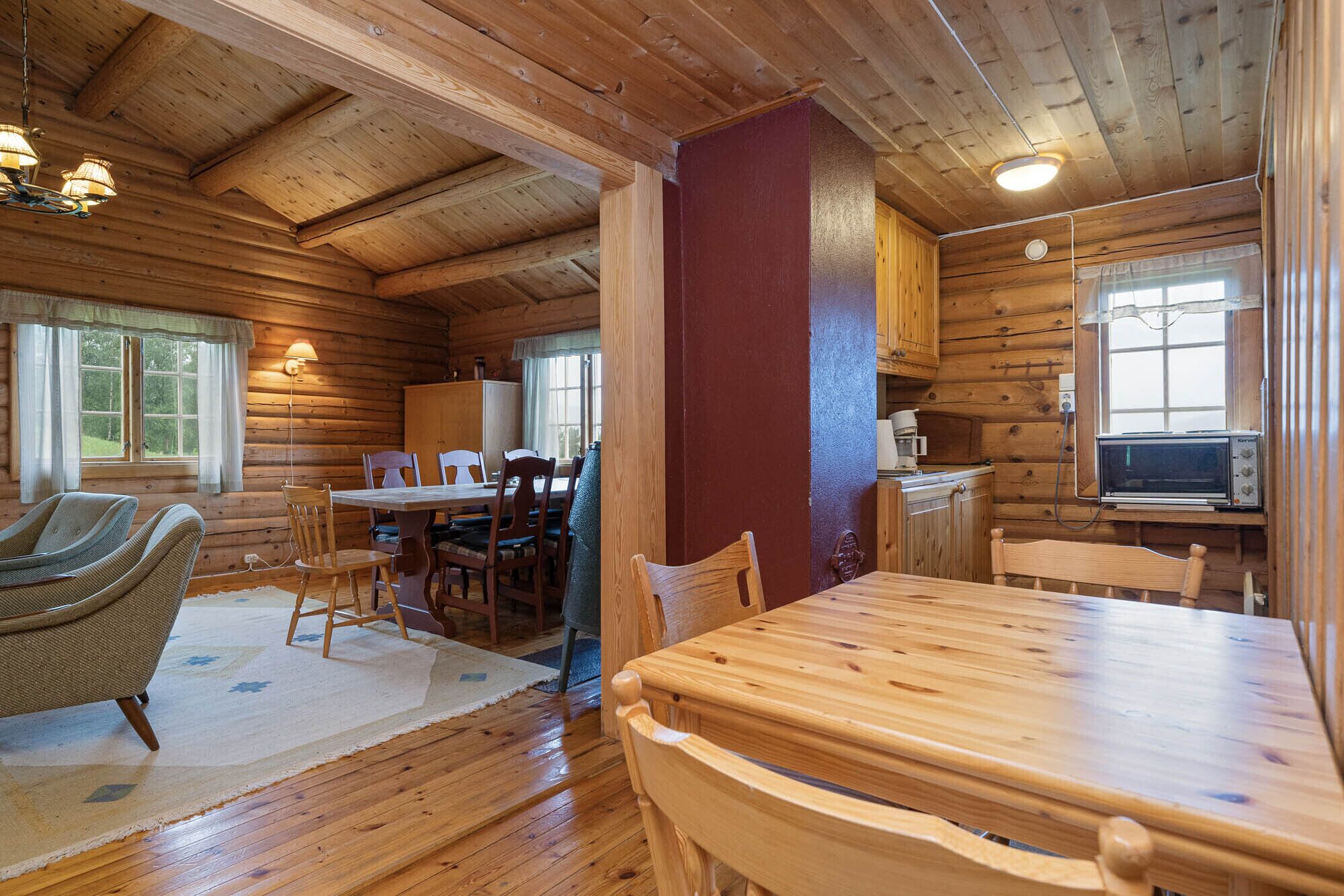 A wooden cabin interior with a dining area, a kitchen with a microwave, and a cozy seating area with a rug.