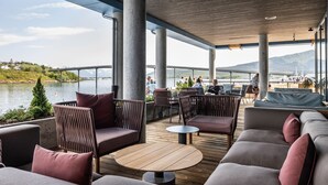 An outdoor seating area with sofas and chairs, a round table, and a view of a river and mountains. - Quality Hotel Richard With (Hadsel)