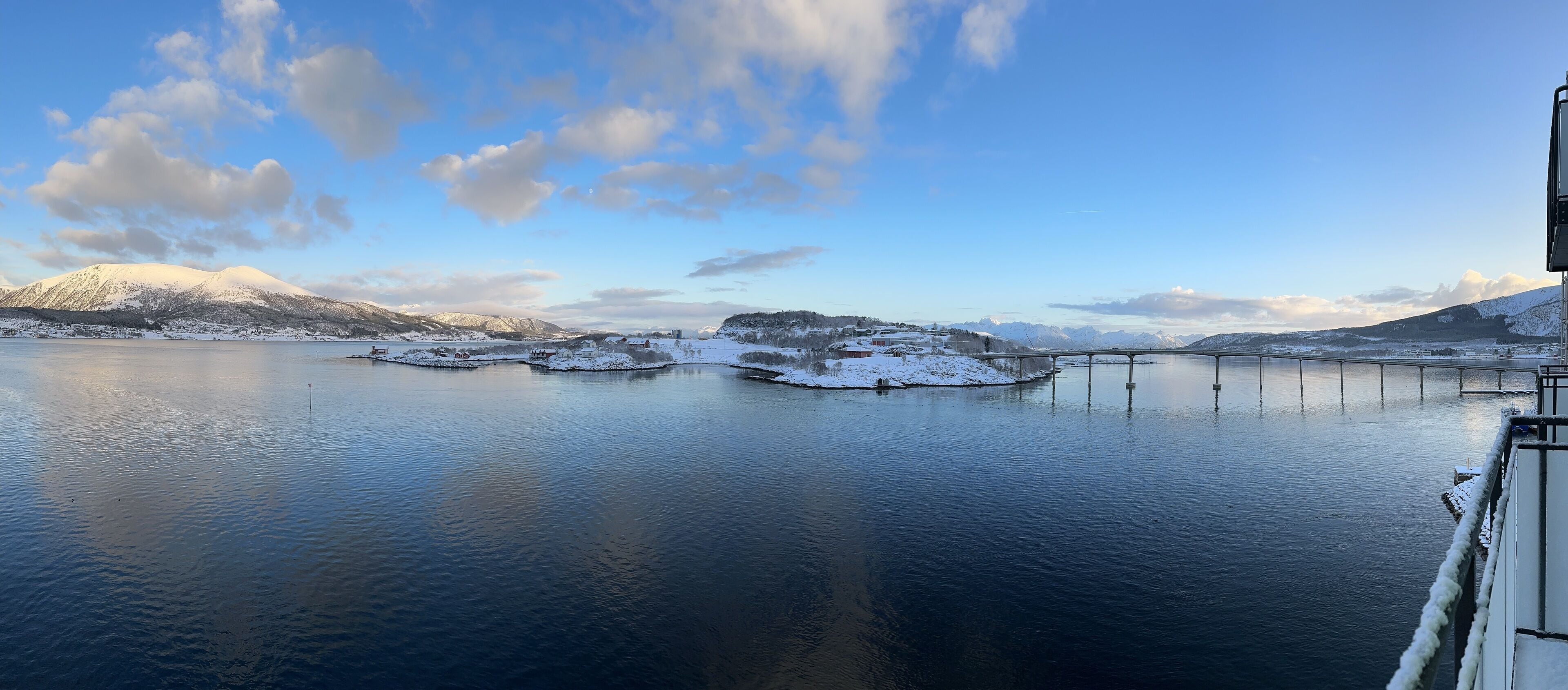 A calm lake with snow-covered islands and mountains in the background.