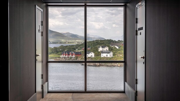 A room with a large window offering a view of a lake and houses across the water. - Quality Hotel Richard With (Hadsel)