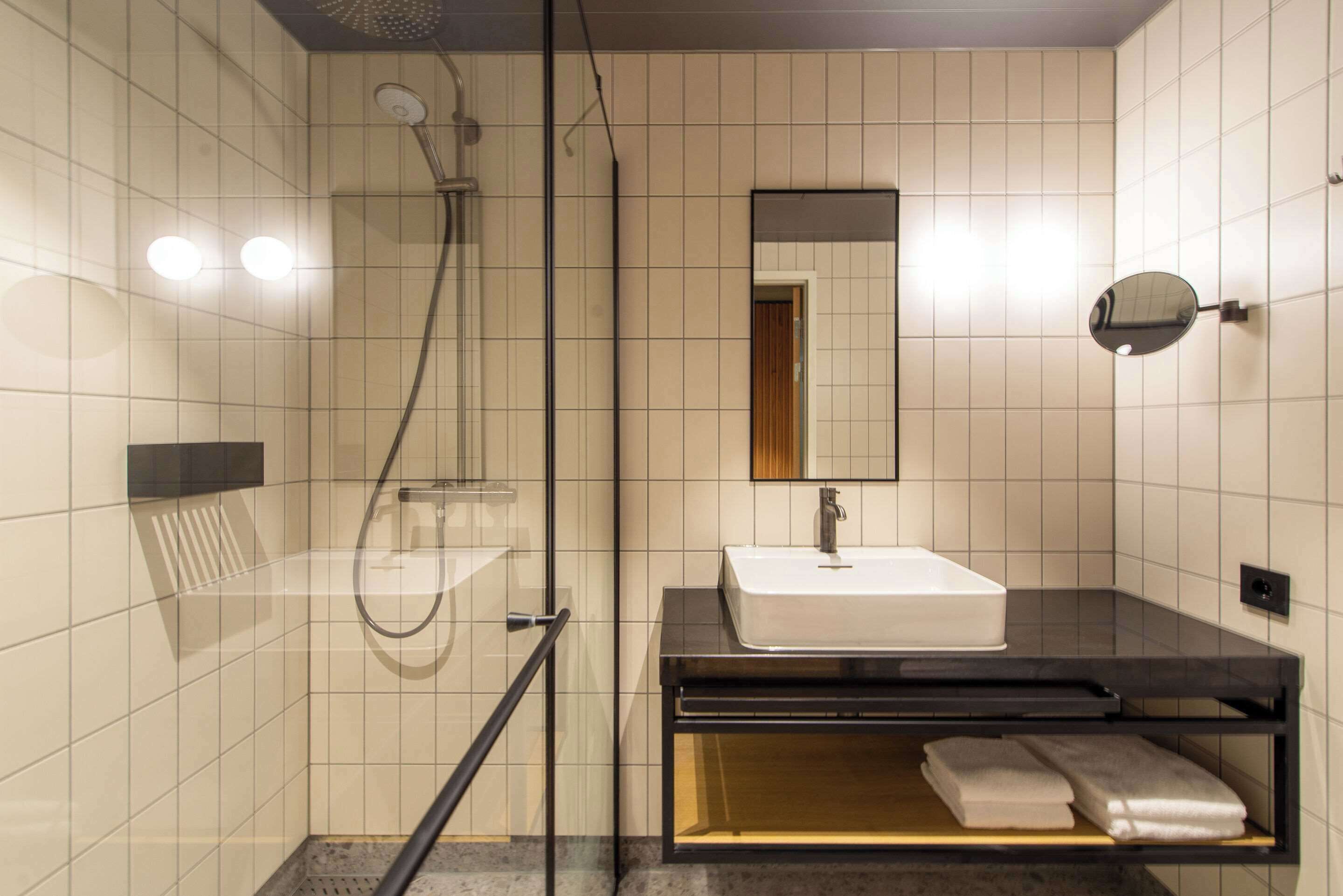 Een moderne badkamer met een douchecabine van glas, een wit wastafeltje en een spiegel.