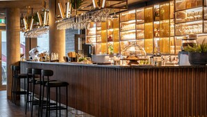 A bar area with a wooden counter, bar stools, hanging glasses, and a variety of bottles and glasses. - Quality Hotel Richard With (Hadsel)