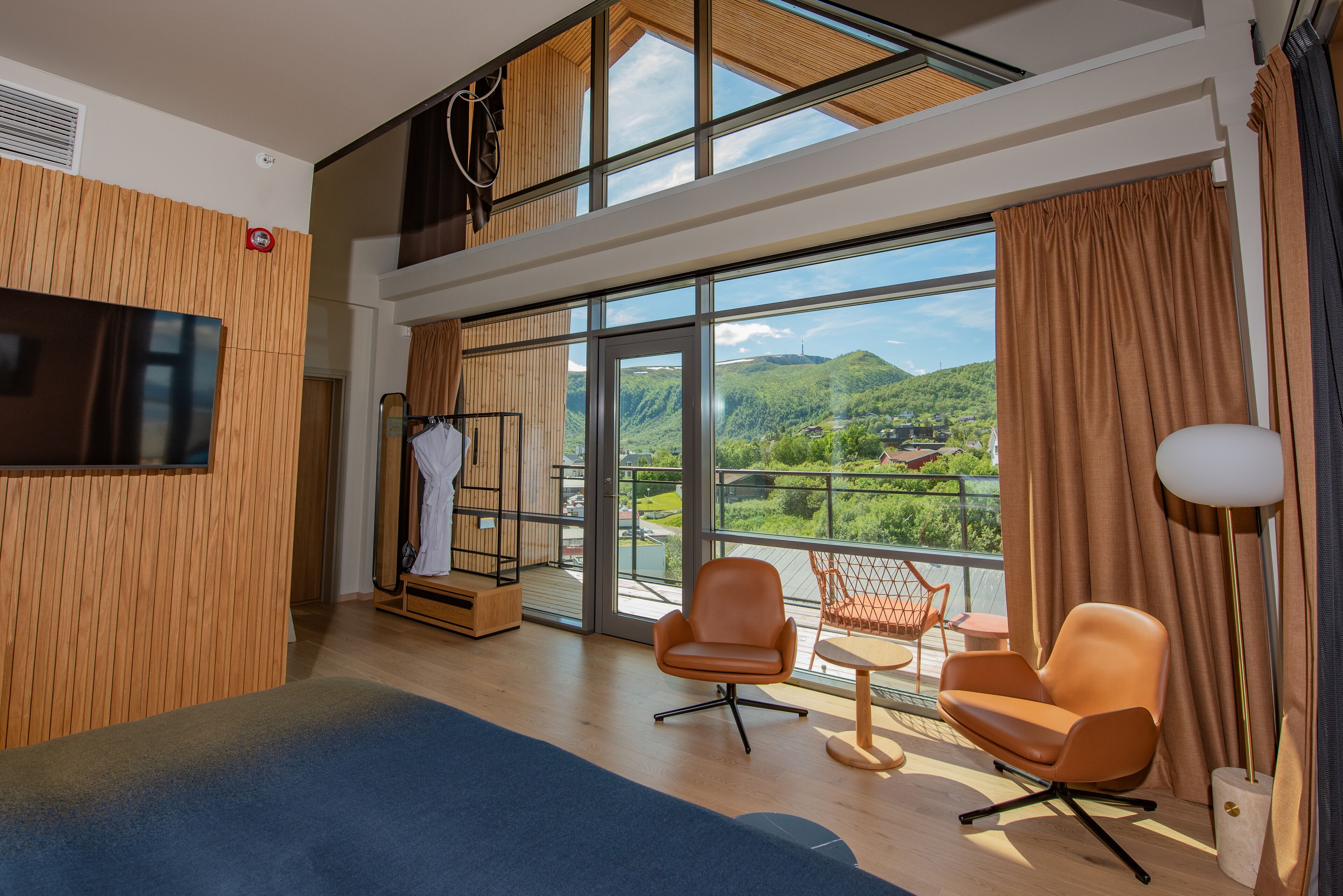 Habitación de hotel moderna con un balcón grande, televisión, zona de estar y vistas a la montaña.