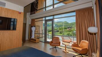 Habitación de hotel moderna con un balcón grande, televisión, zona de estar y vistas a la montaña.
