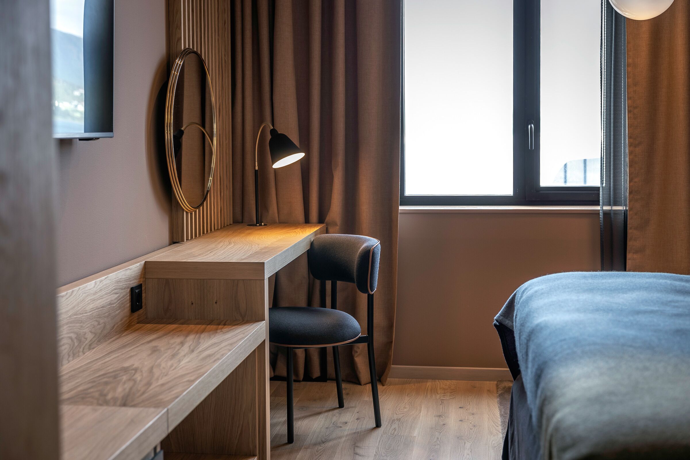 Een moderne hotelkamer met een houten bureau, een stoel, een bed, een televisie en een raam met gordijnen.