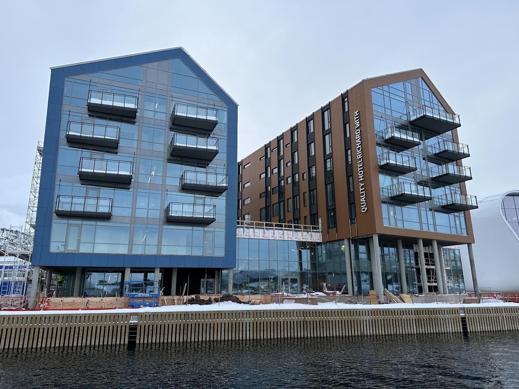 Un hôtel moderne doté d’une façade en verre, de nombreux balcons et offrant une vue dégagée sur l’eau.