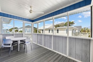 Uma área externa coberta com mesa e cadeiras, grandes janelas e vista para casas.