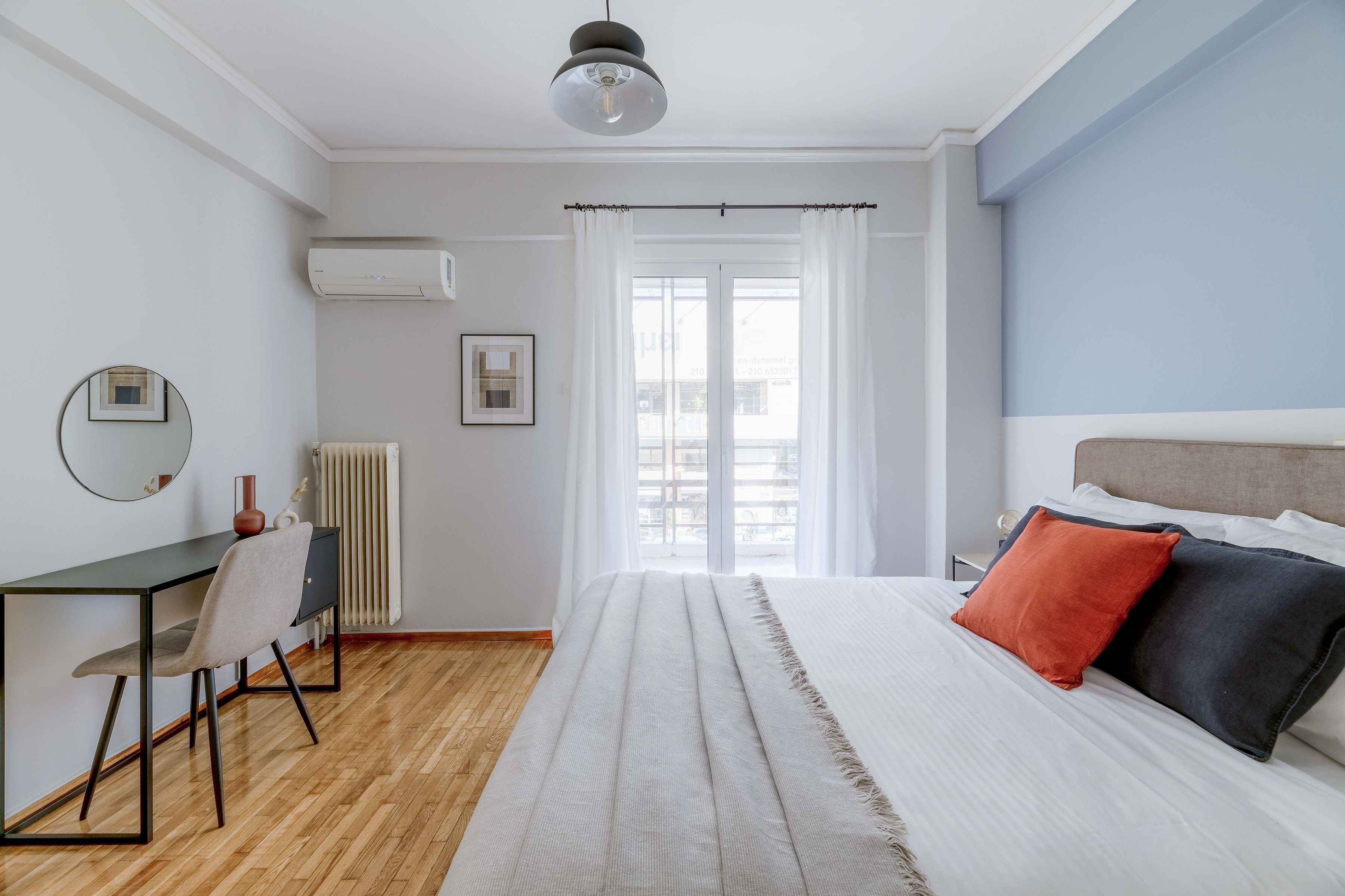 A bedroom with a bed, a desk, a chair, a radiator, and a window with curtains.