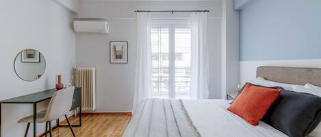 A bedroom with a bed, a desk, a chair, a radiator, and a window with curtains.