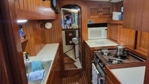 A compact kitchen with wooden cabinets, a microwave, a stove, and a sink. - WindSong: A charming 3-bedroom retreat in Boothbay Harbor, ME, near waterfront views. (Boothbay Harbor)
