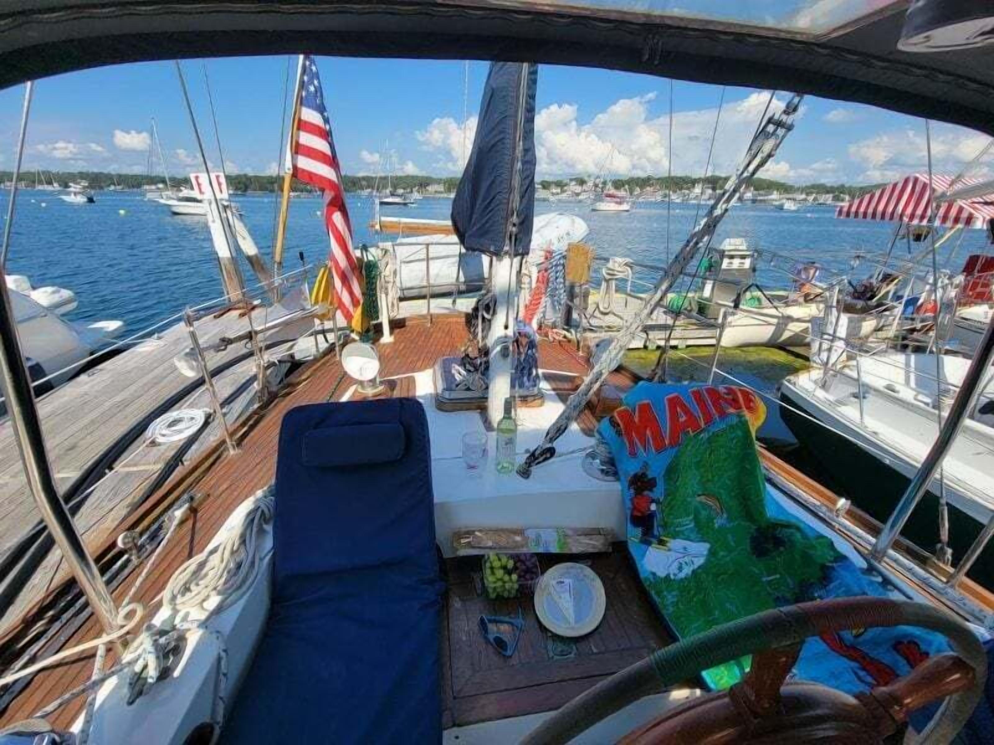 Een scheepdek met een stuurwiel, een Amerikaanse vlag en een bord met de tekst 'MAINE'.