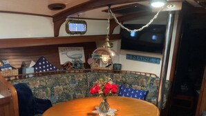 A cabin interior with a round wooden table, floral-patterned bench, a vintage television, and a 'J MAINE' sign. - WindSong: A charming 3-bedroom retreat in Boothbay Harbor, ME, near waterfront views. (Boothbay Harbor)