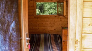 Interior de una cabaña de madera con una cama, una ventana y una puerta.