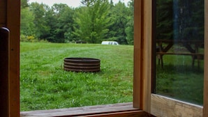 Un piso de madera que conduce a una puerta de cristal con vistas a un campo cubierto de hierba y árboles.