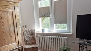 Ein Schlafzimmer mit Bett, Stuhl, Heizkörper, Fernseher und einem Fenster mit Jalousien.