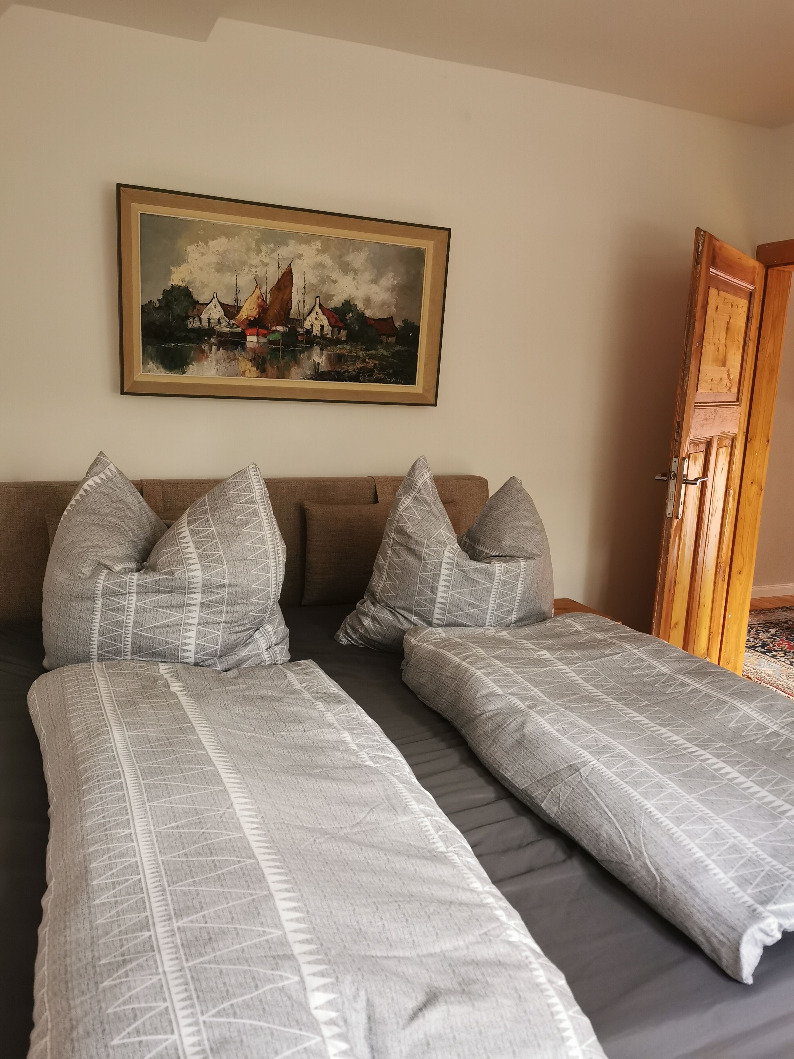 Un letto matrimoniale con biancheria a motivi, un quadro raffigurante un paesaggio di un villaggio e un armadio in legno.
