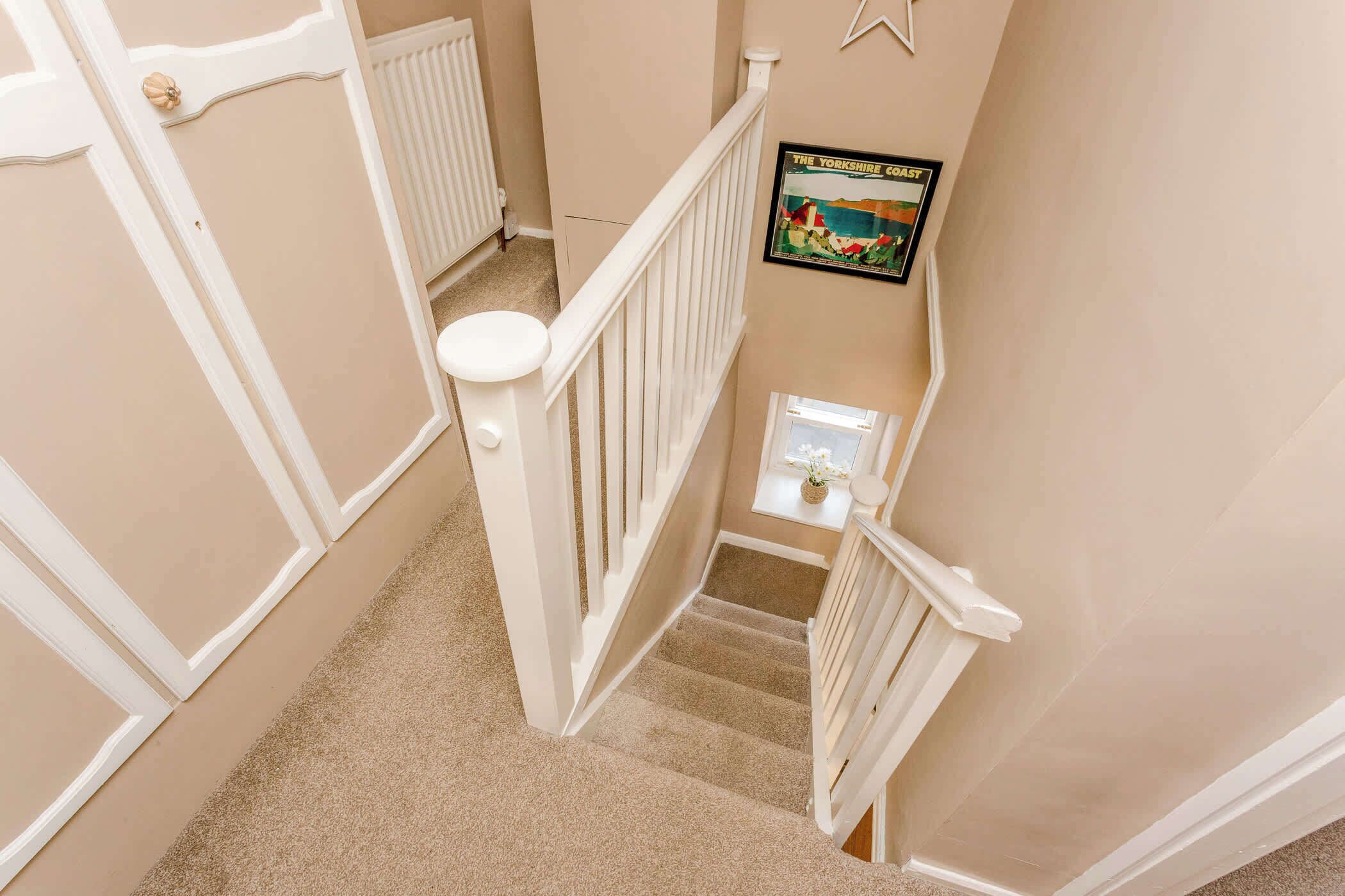 A carpeted staircase with white railings and a framed picture on the wall.