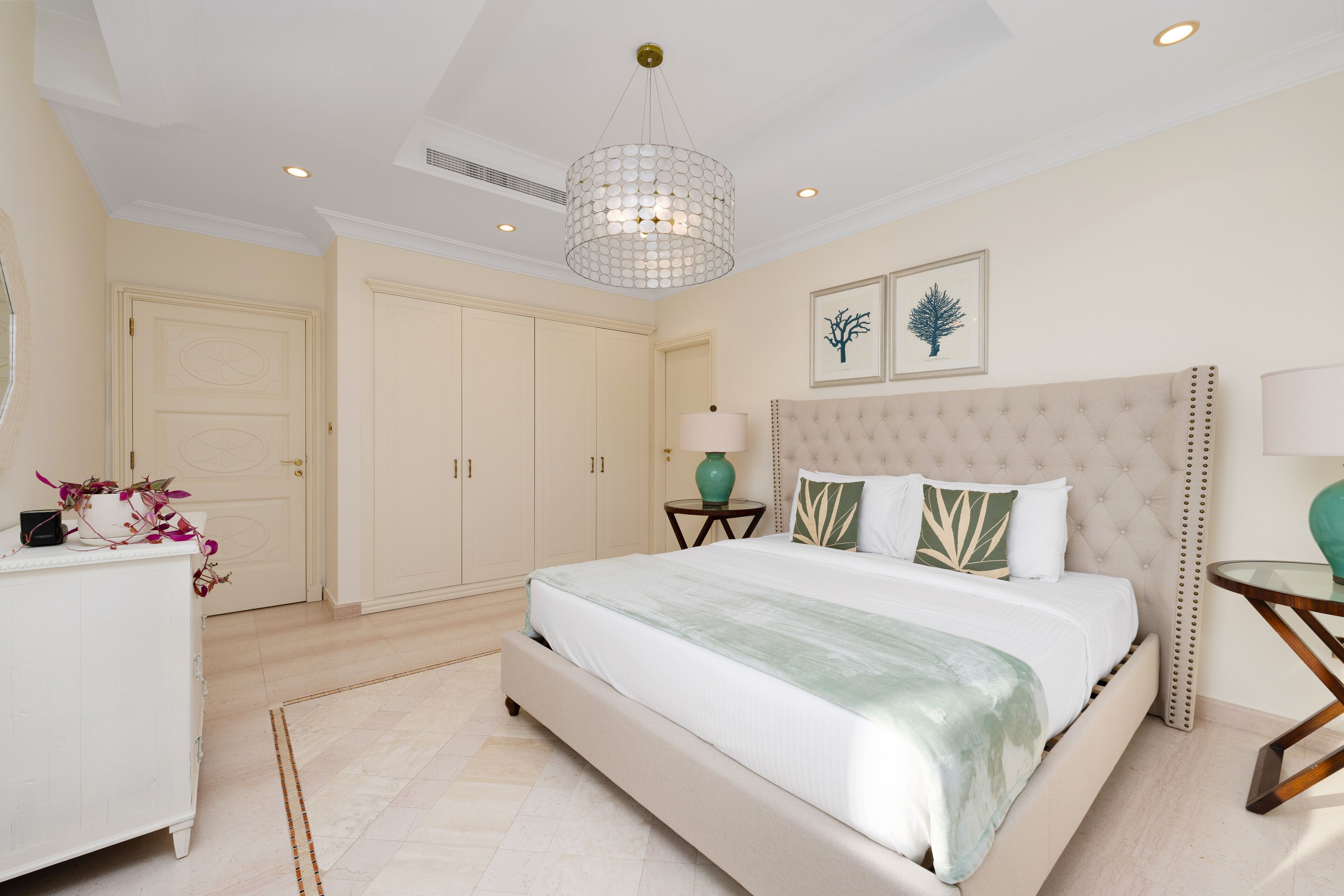 A bedroom with a large bed, a chest of drawers, a bedside table, and a hanging light fixture.