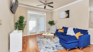 A living room with a blue sofa, a white coffee table, a ceiling fan, and a TV mounted on the wall. - MD Anderson Med Center  Free Parking (Houston)