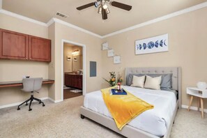 Cozy retreat with a large bed, desk, and chair, featuring a ceiling fan and a window.