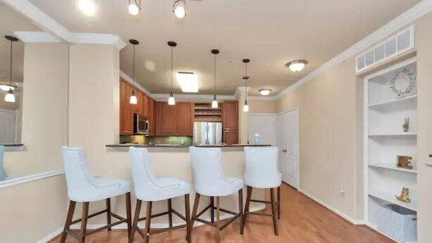 A modern kitchen with wooden cabinets, a central island, and bar stools. - MD Anderson Med Center  Free Parking (Houston)