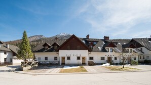 A row of traditional chalet-style buildings with sloped roofs, set against a backdrop of mountains and clear sky. - Our Second Home (Kranjska Gora)