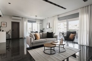 Ein modernes Wohnzimmer mit einer Couch, einem Couchtisch und Blick auf die Stadt durch große Fenster.