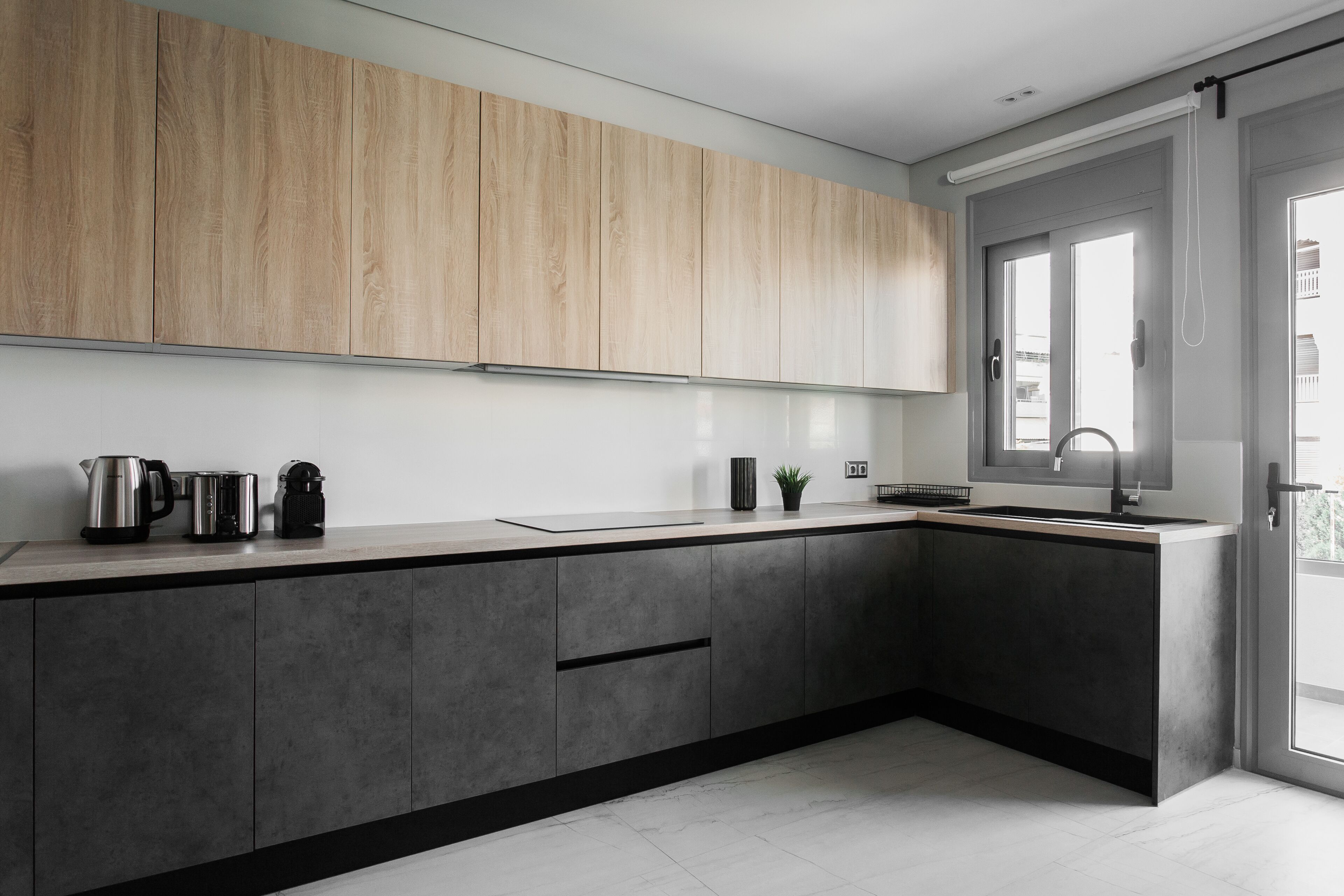 A modern kitchen with grey cabinets, a stainless steel kettle, a coffee maker, and a sink.