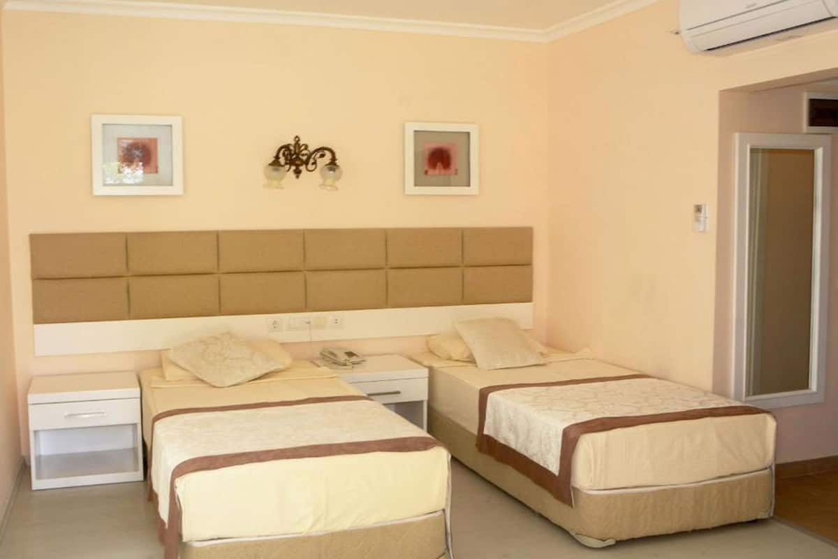 A hotel room with two beds, a bedside table, a nightstand, and an air conditioning unit.
