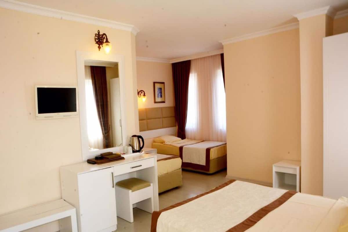 A hotel room with a bed, a desk with a chair, a bedside table, a TV, and a window with curtains.