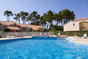 Una piscina con sillas de descanso, un área cercada y edificios con tejados de tejas.