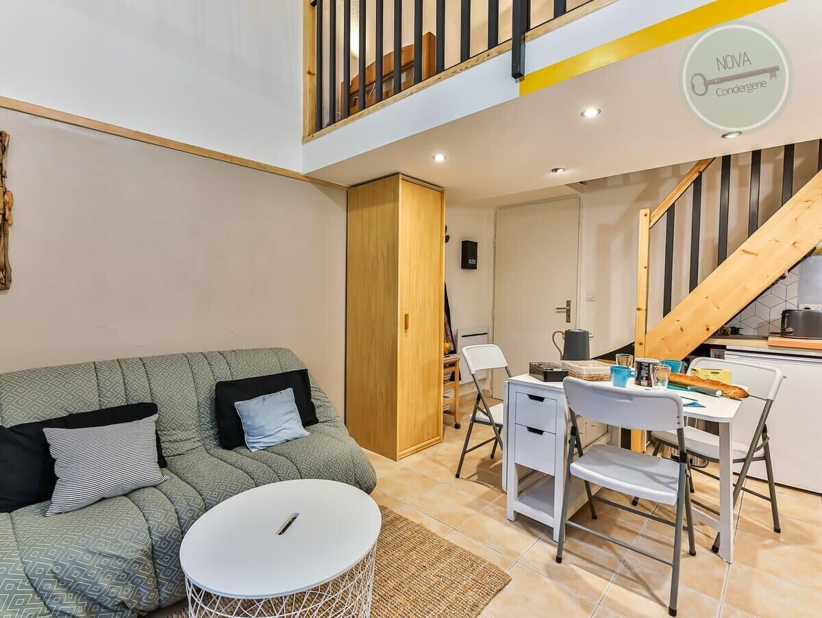 A modern living room with a sofa, a dining table, and a kitchen area with a wooden staircase.