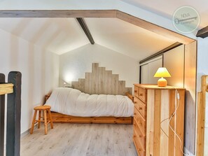 A bedroom with a sloped ceiling, a bed with a wooden headboard, a nightstand with a lamp, and a dresser.