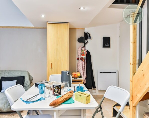 Un espace de vie compact comprenant une table à manger, un coin cuisine, un canapé et un porte-manteau.