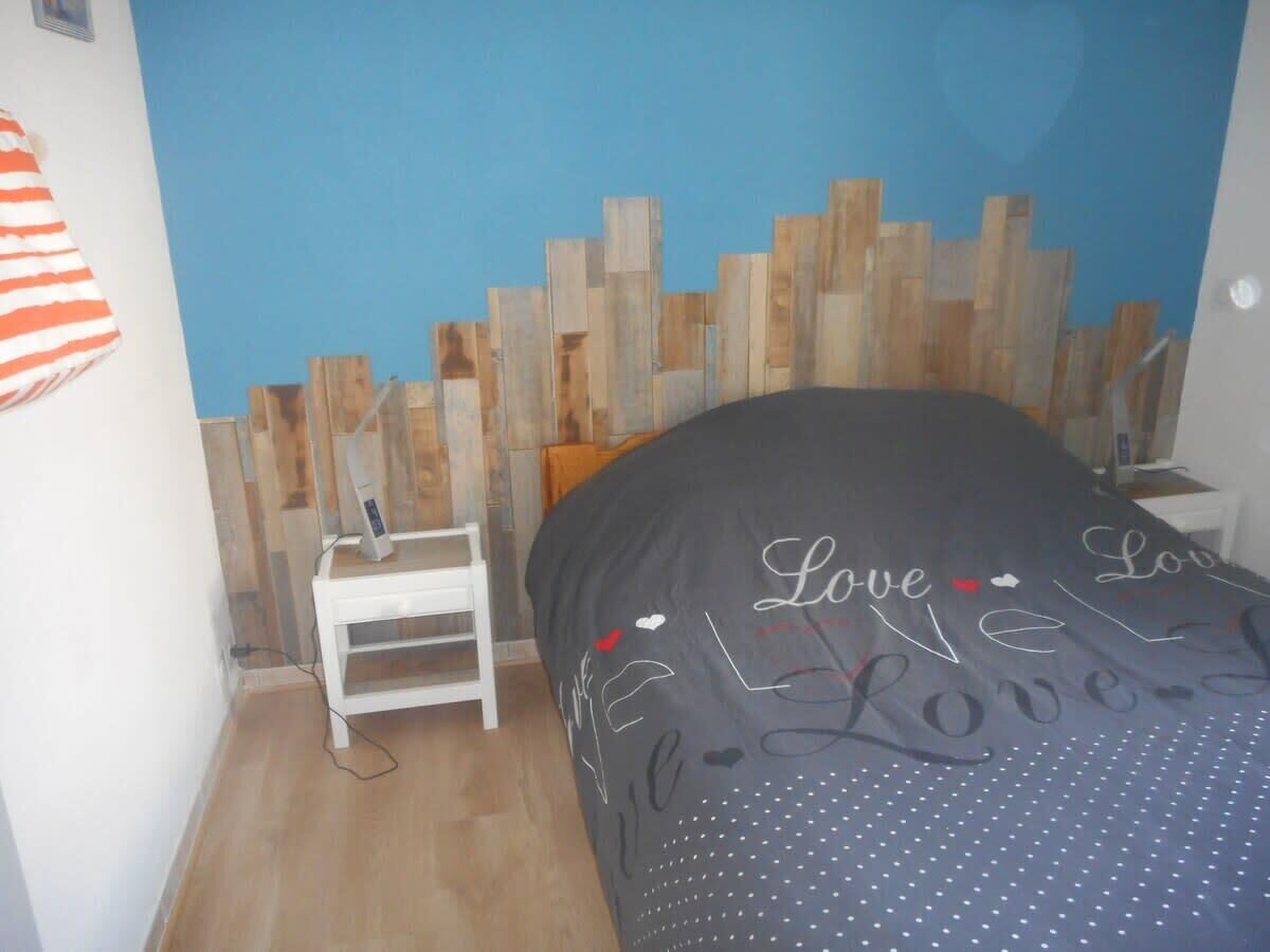A bedroom with a bed, a white nightstand, and a blue wall.