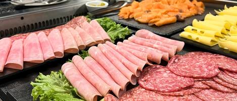 A variety of meats and vegetables on a tray, with a water dispenser and a wooden box labeled "SANTI" in the background.