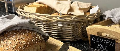 Una barra de pan sobre una tabla de cortar con un cuchillo, una cesta de pan y un cartel que dice 'GLUTEN FREE'.